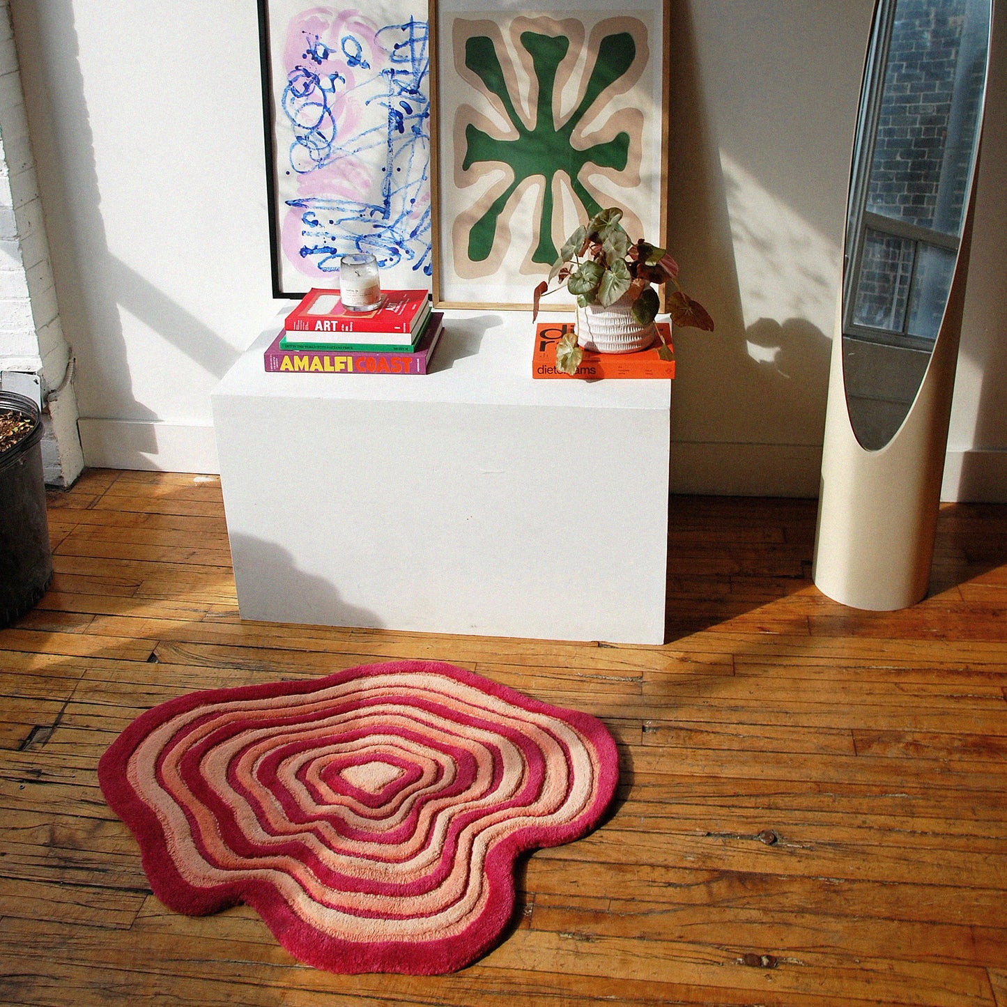 Our portal rug styled in a stylish modern setup. It is in front of a vintage white lipstick mirror, and a white table styled  with 4 books, a plant, candle, and 2 framed abstract art pieces on top
